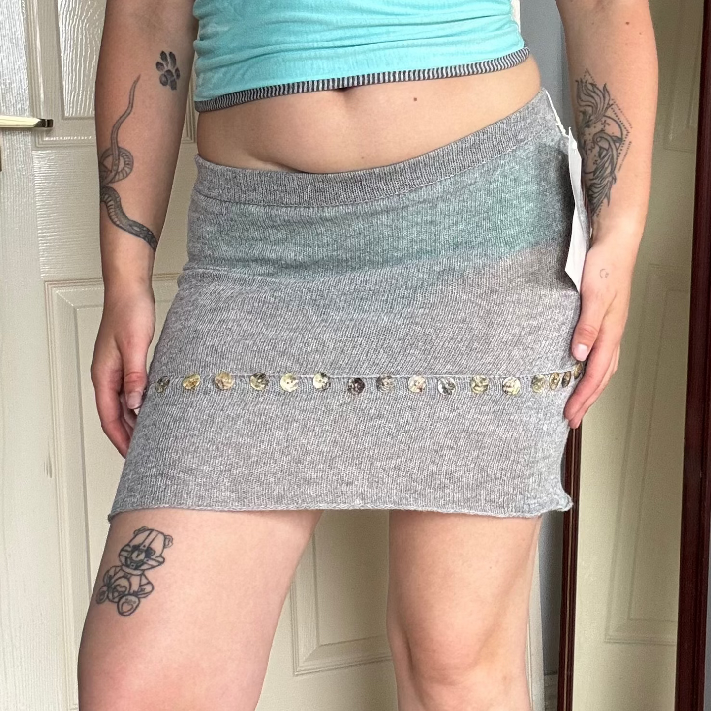 Person wearing a grey knit mini skirt with pearl button details.
