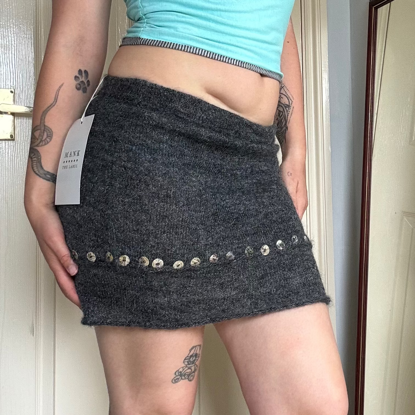 Person wearing a grey knit mini skirt with pearl button details.