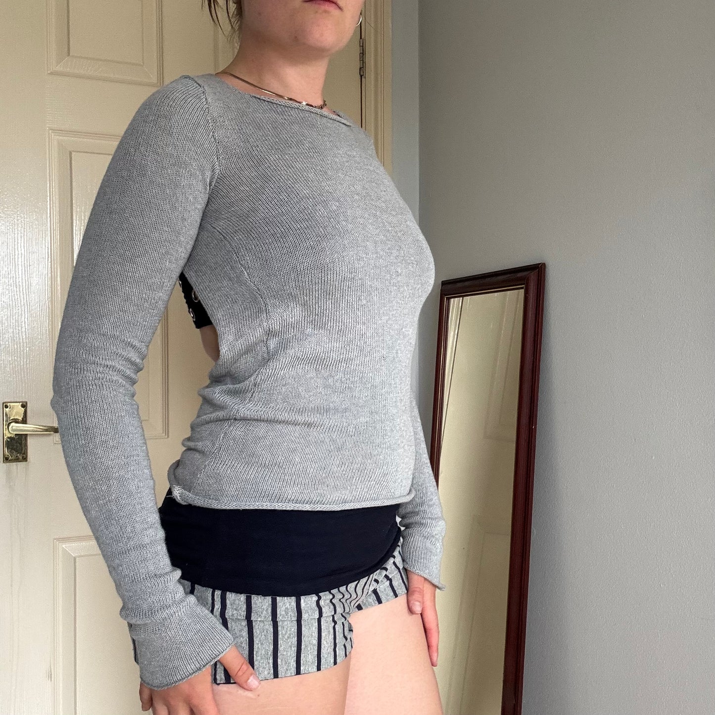 Person wearing a gray knit long sleeve backless top with striped shorts.