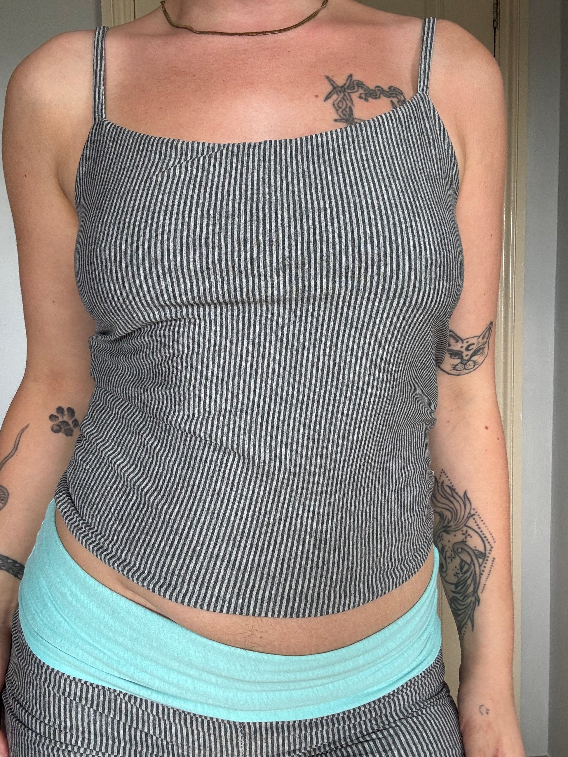 Person wearing a light blue / turquoise and grey stripe reversible tank top.