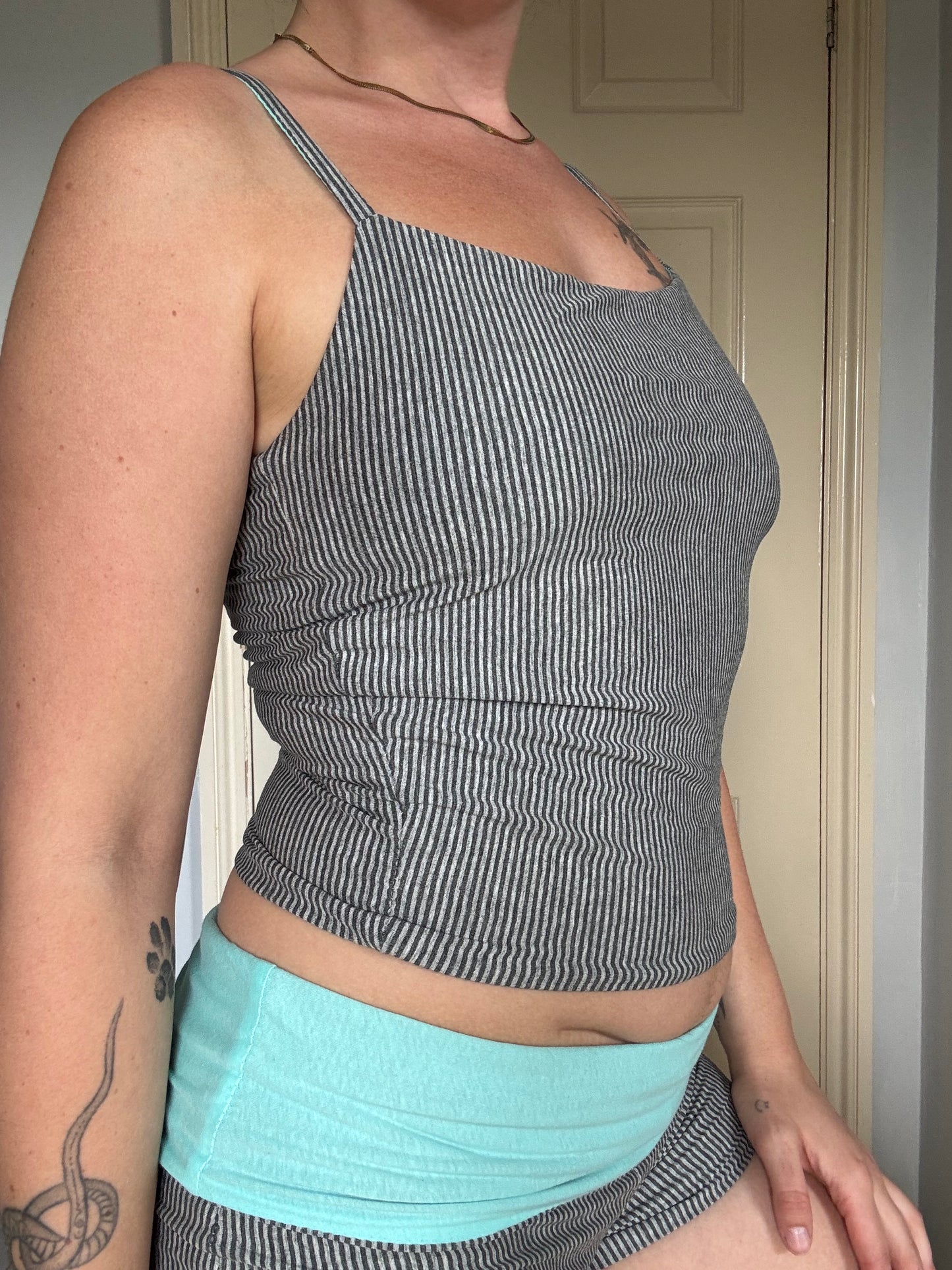 Person wearing a light blue / turquoise and grey stripe reversible tank top.