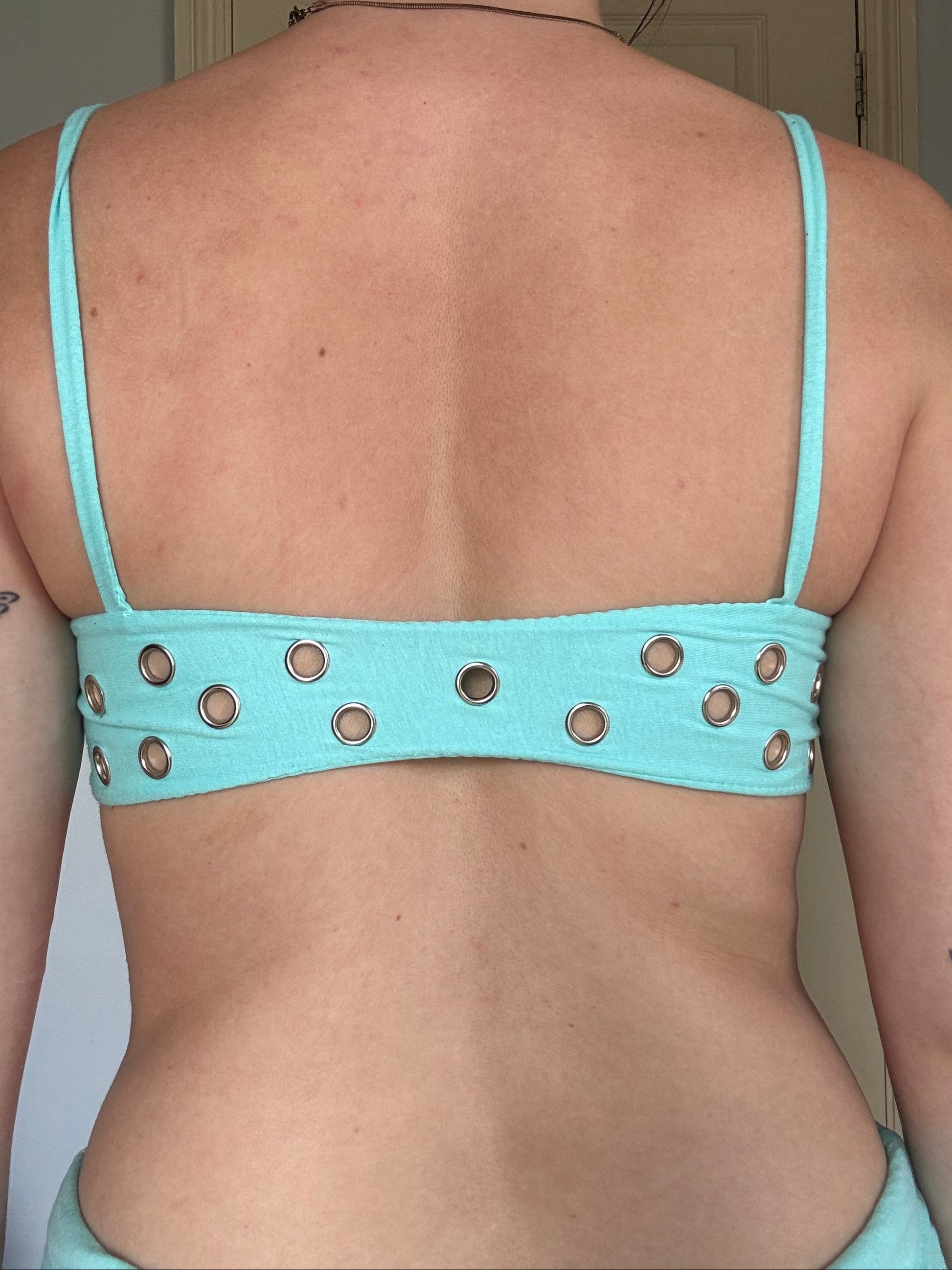 person wearing a turquoise cotton eyelet bralet with hanging brand tag.