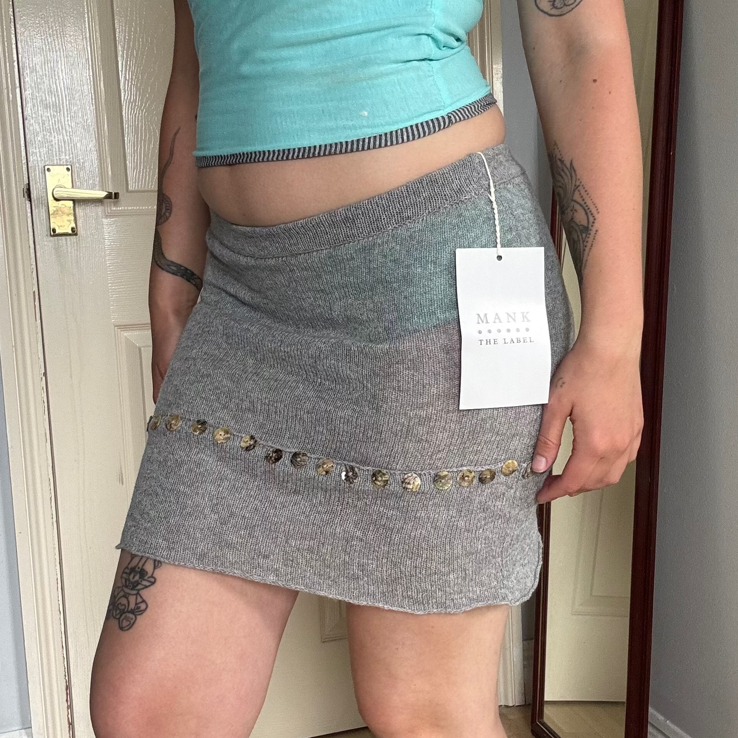 Person wearing a grey knit mini skirt with pearl button details.