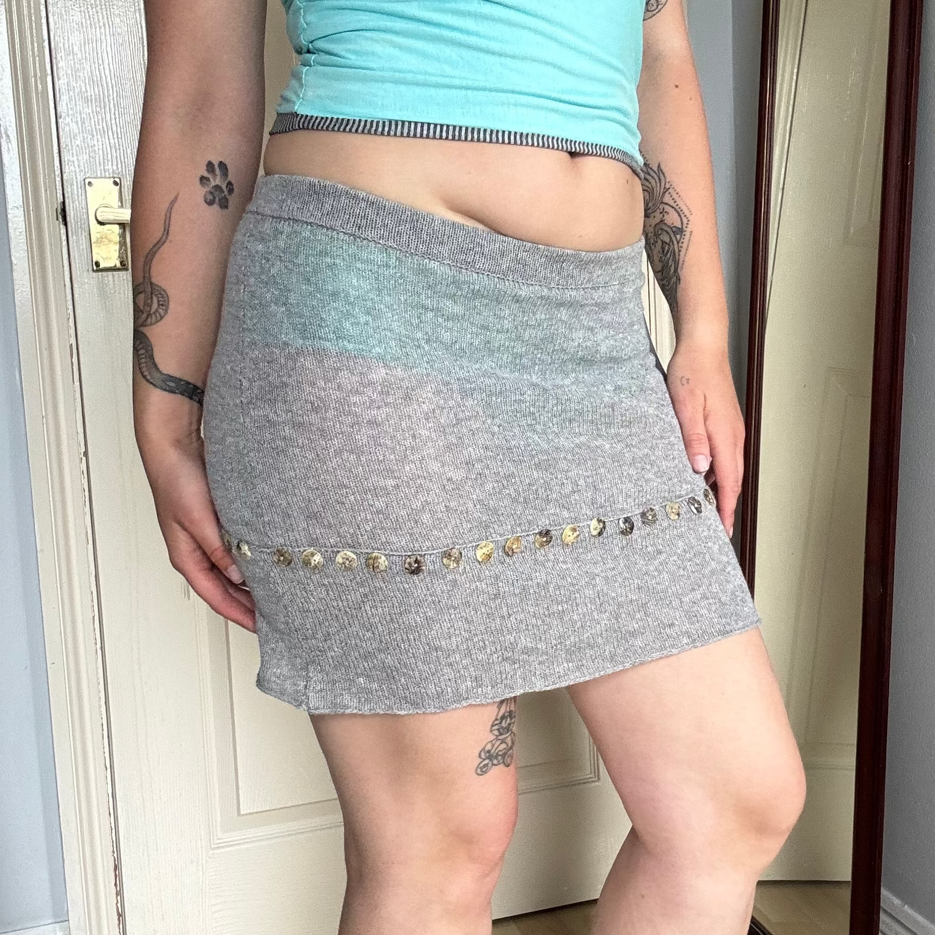 Person wearing a grey knit mini skirt with pearl button details.