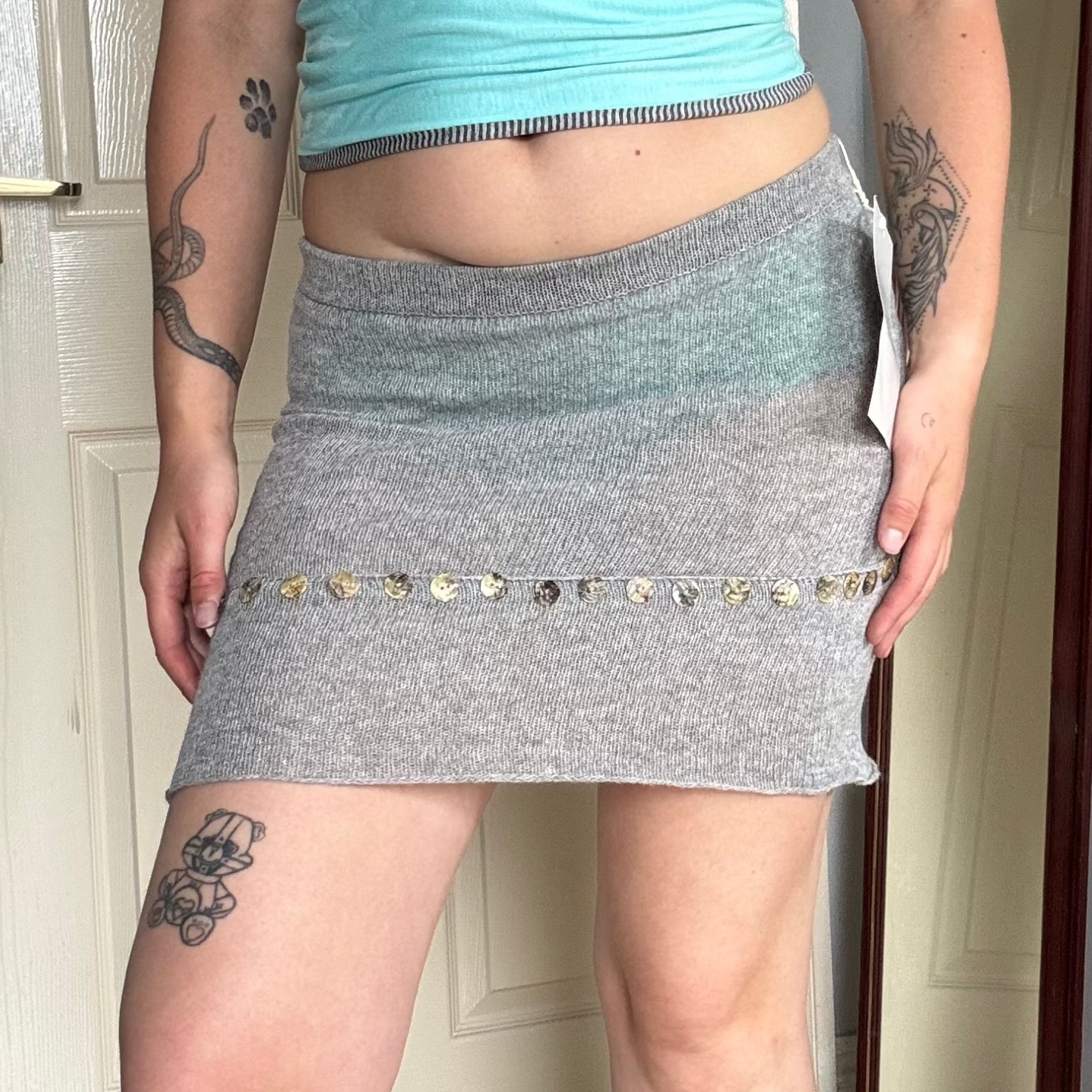 Person wearing a grey knit mini skirt with pearl button details.