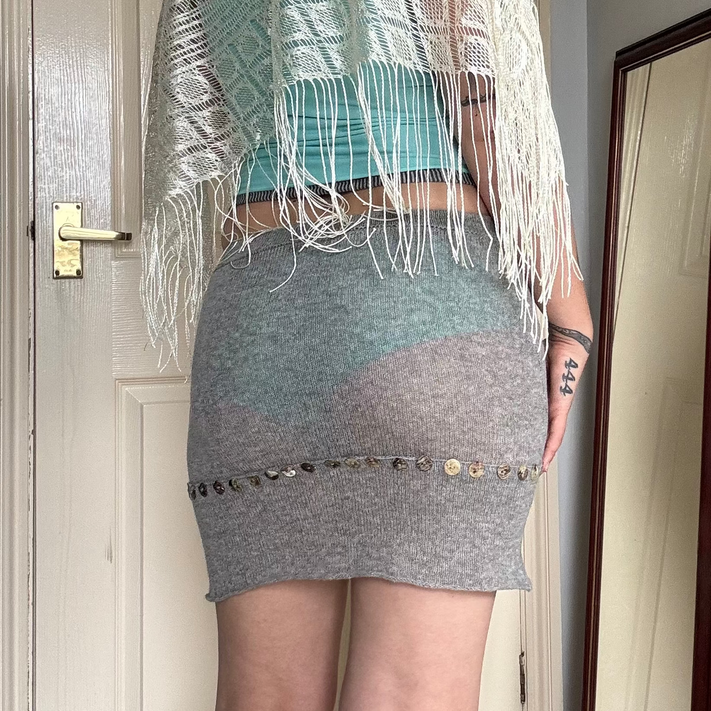 Person wearing a grey knit mini skirt with pearl button details.
