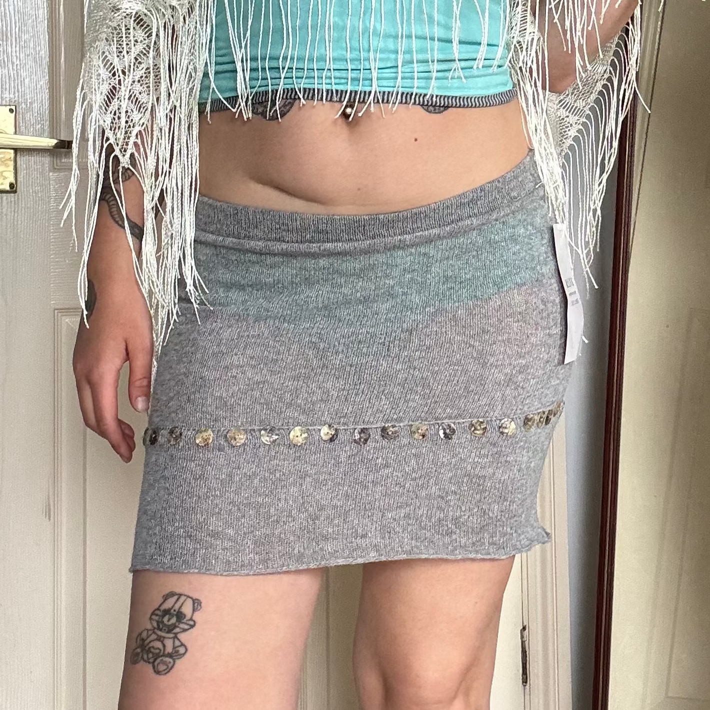 Person wearing a grey knit mini skirt with pearl button details.