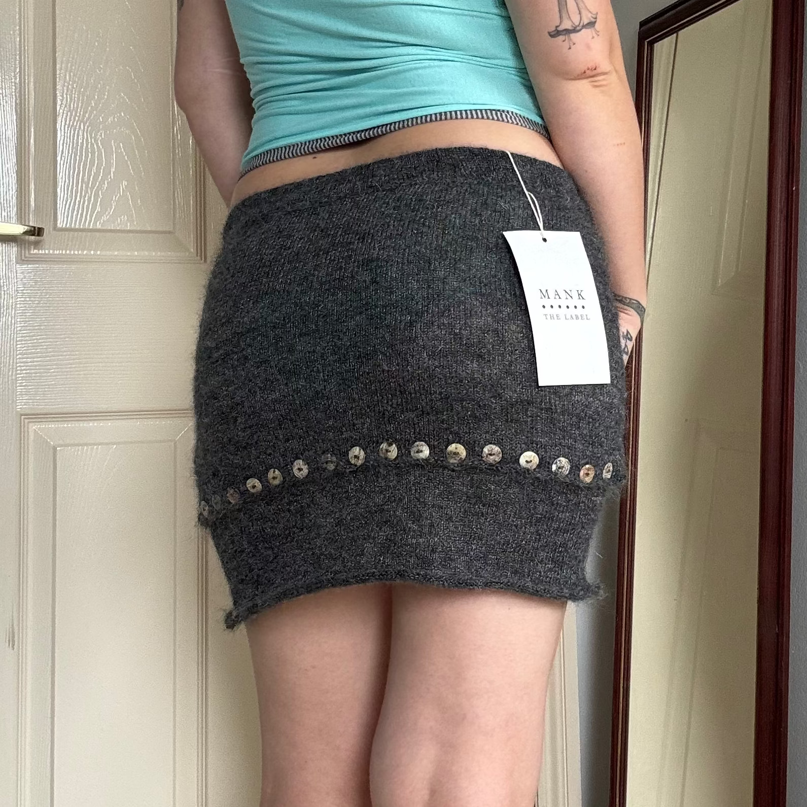 Person wearing a grey knit mini skirt with pearl button details.