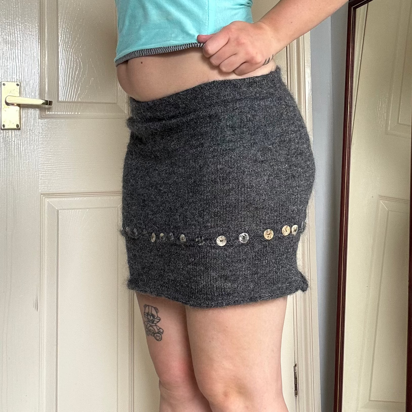 Person wearing a grey knit mini skirt with pearl button details.