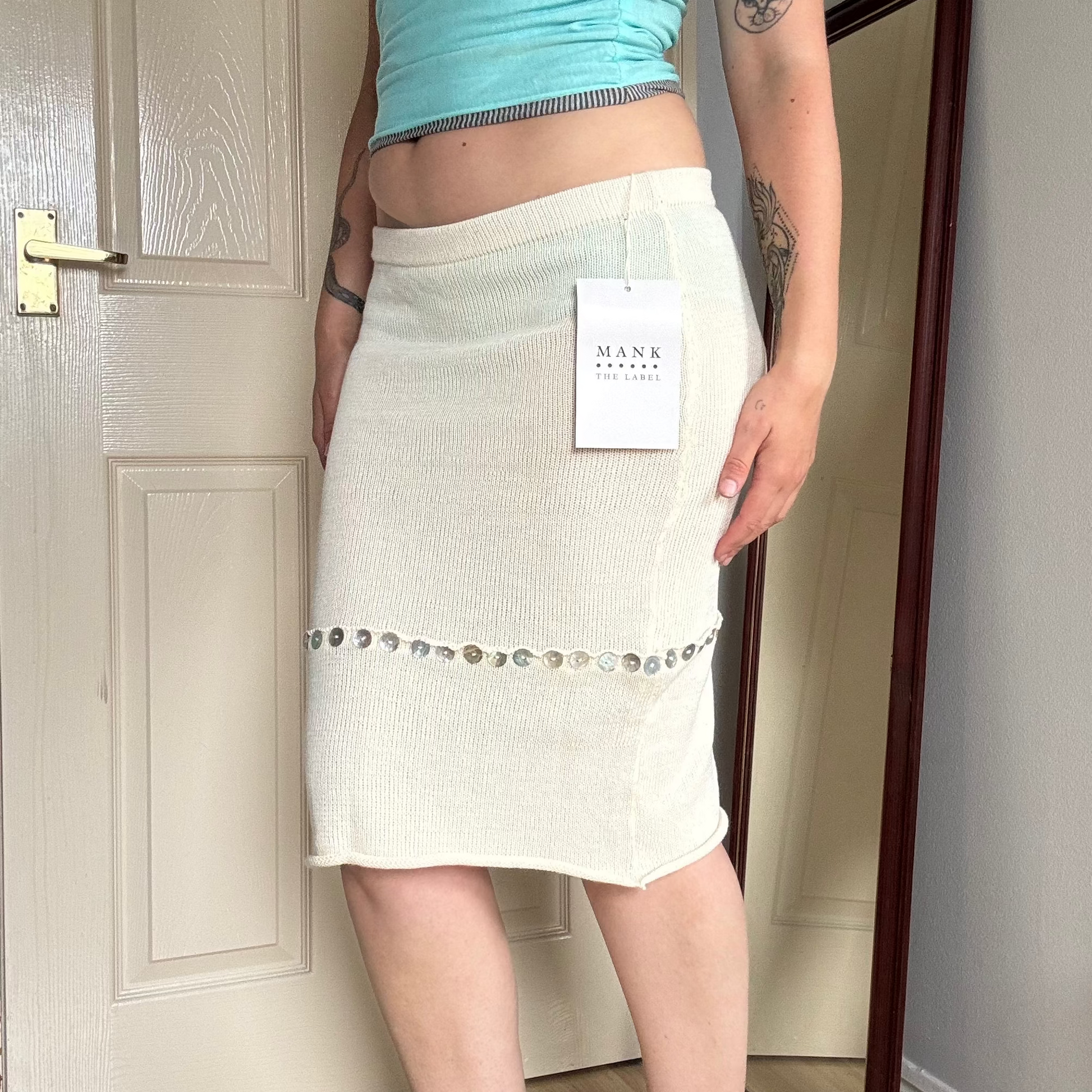 Person wearing a white knit midi skirt with pearl button details.