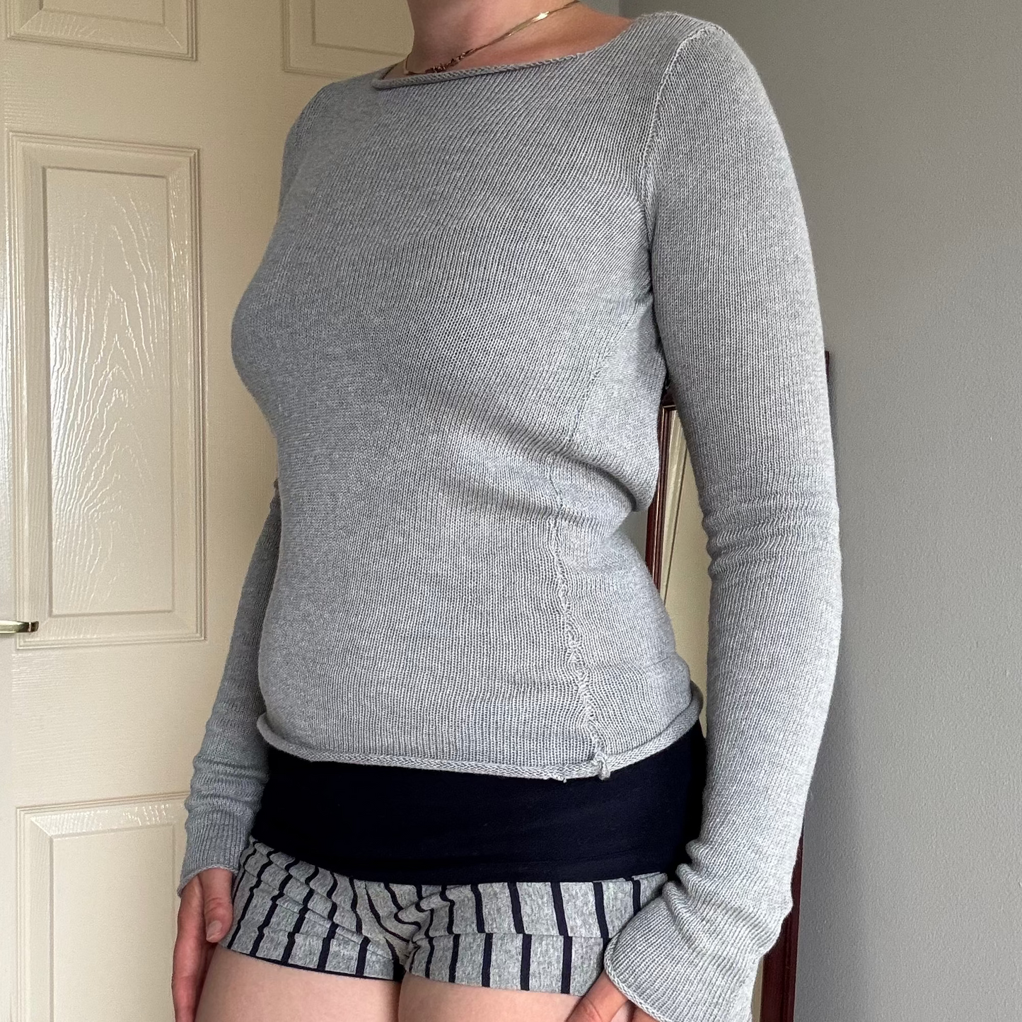 Person wearing a gray knit long sleeve backless top with striped shorts.