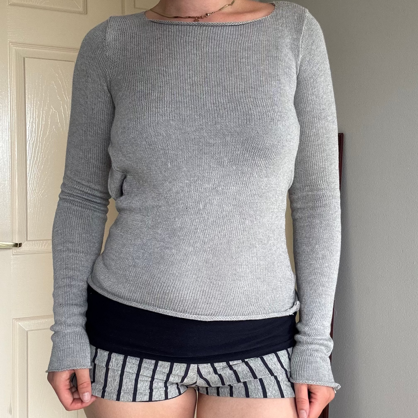 Person wearing a gray knit long sleeve backless top with striped shorts.