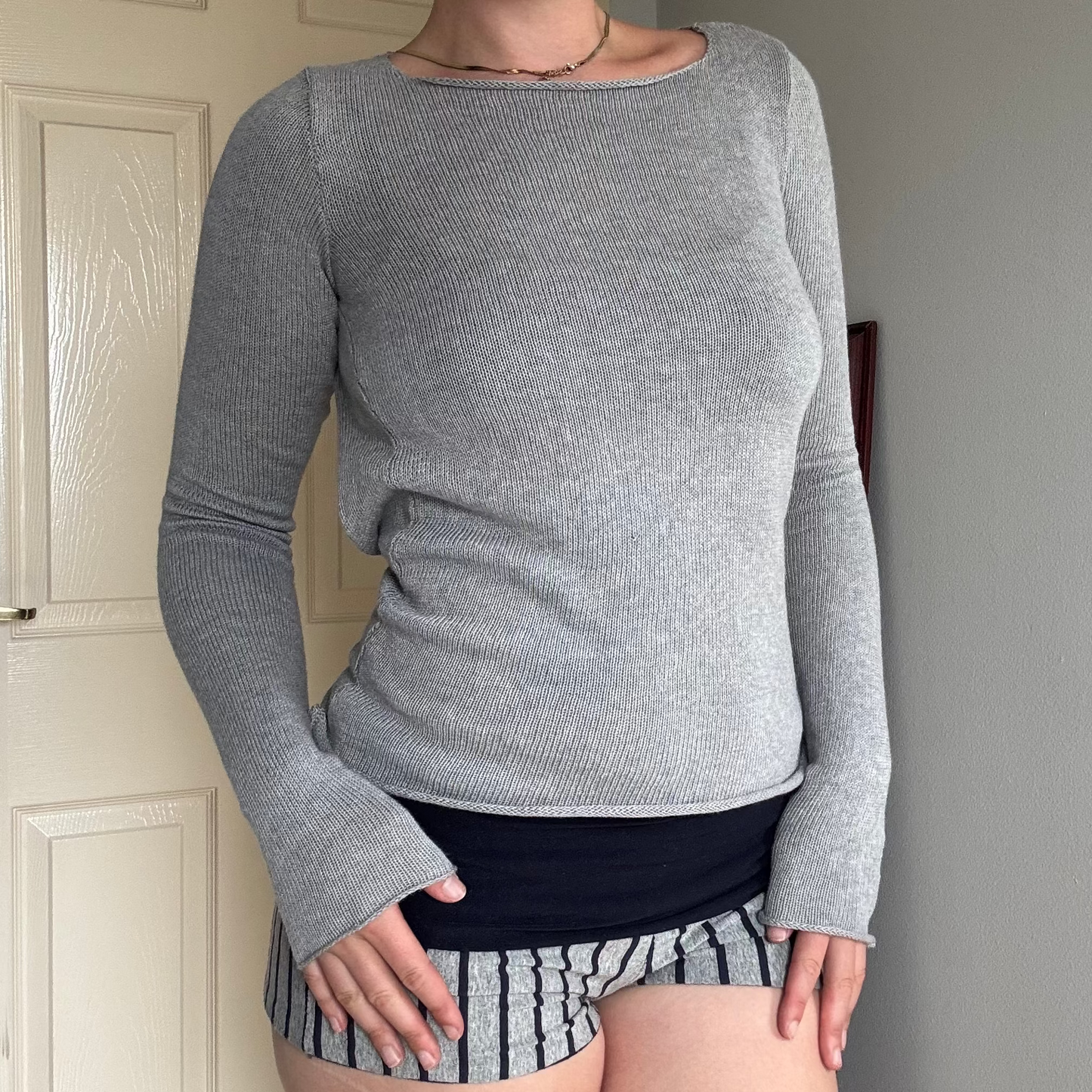 Person wearing a gray knit long sleeve backless top with striped shorts.