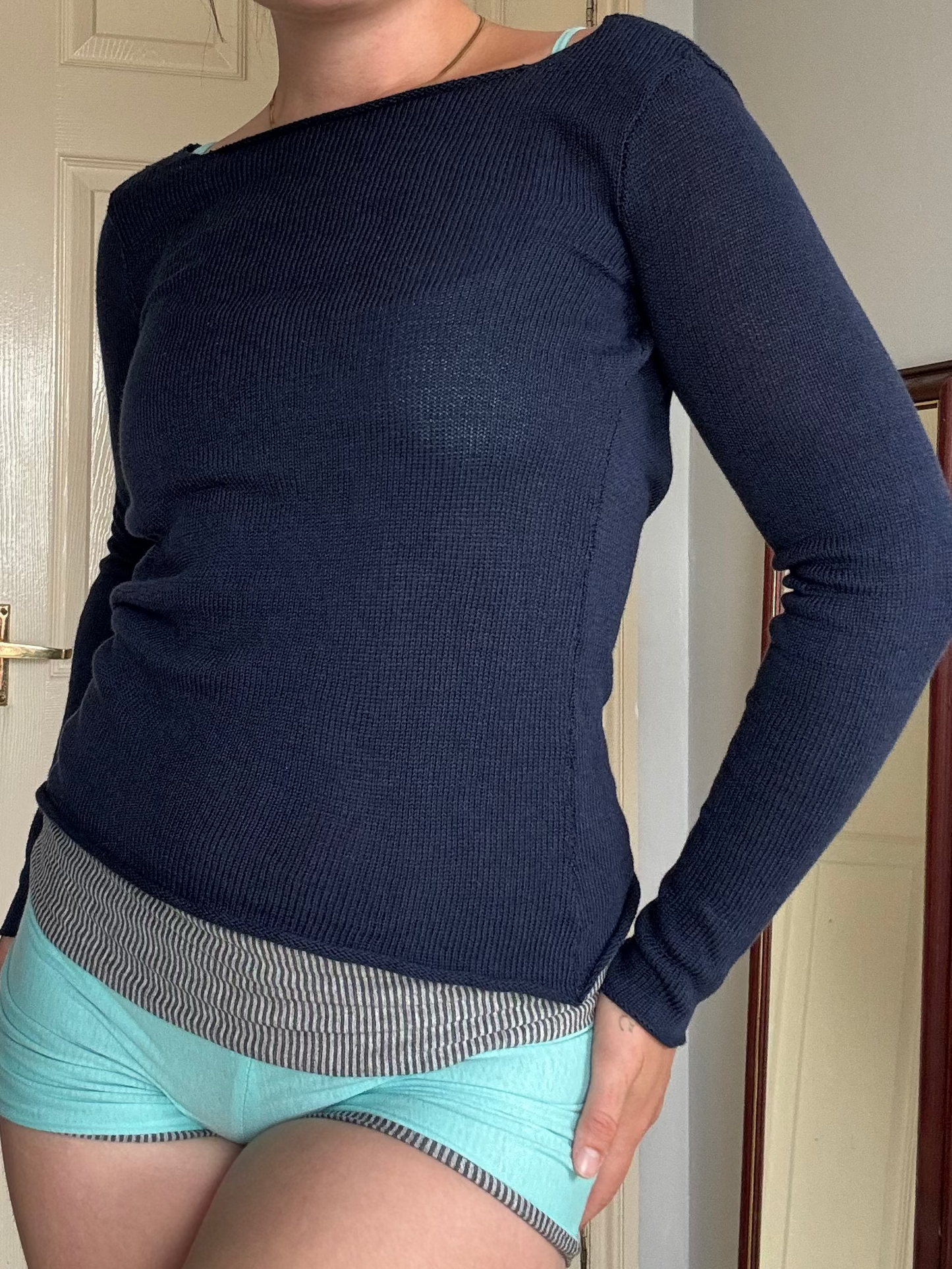Person wearing a navy blue long-sleeve top and light blue shorts in a room.